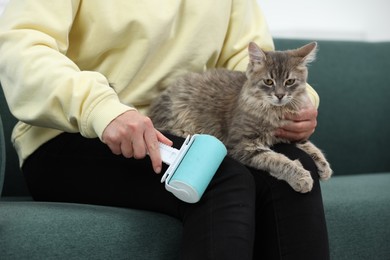 Photo of Pet shedding. Woman with lint roller removing cat`s hair from trousers on sofa at home, closeup