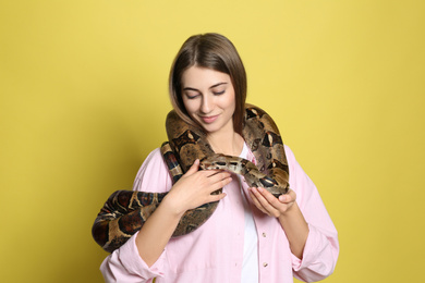 Young woman with boa constrictor on yellow background. Exotic pet