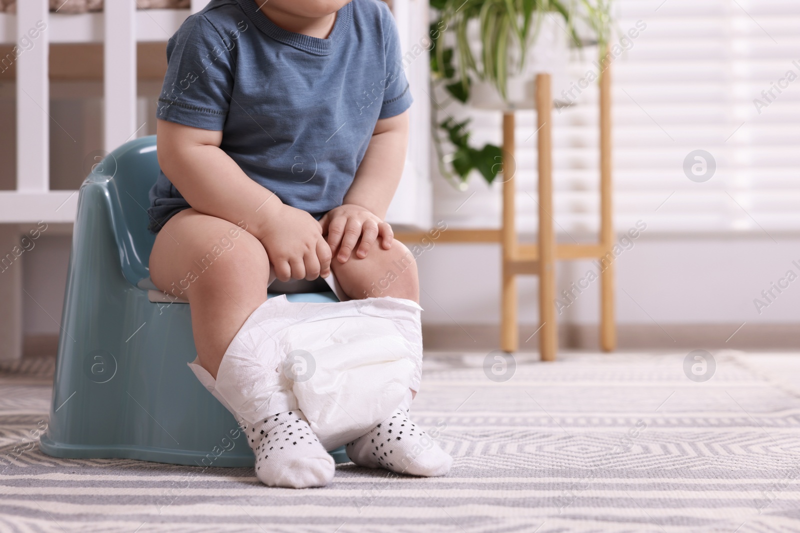 Photo of Little child sitting on plastic baby potty indoors, closeup. Space for text