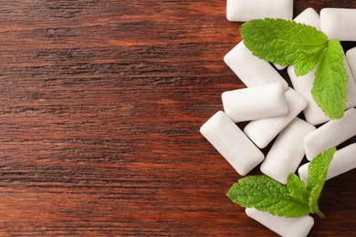 Photo of Tasty white chewing gums and mint leaves on wooden table, top view. Space for text