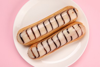 Delicious eclairs covered with glaze on pink background, top view