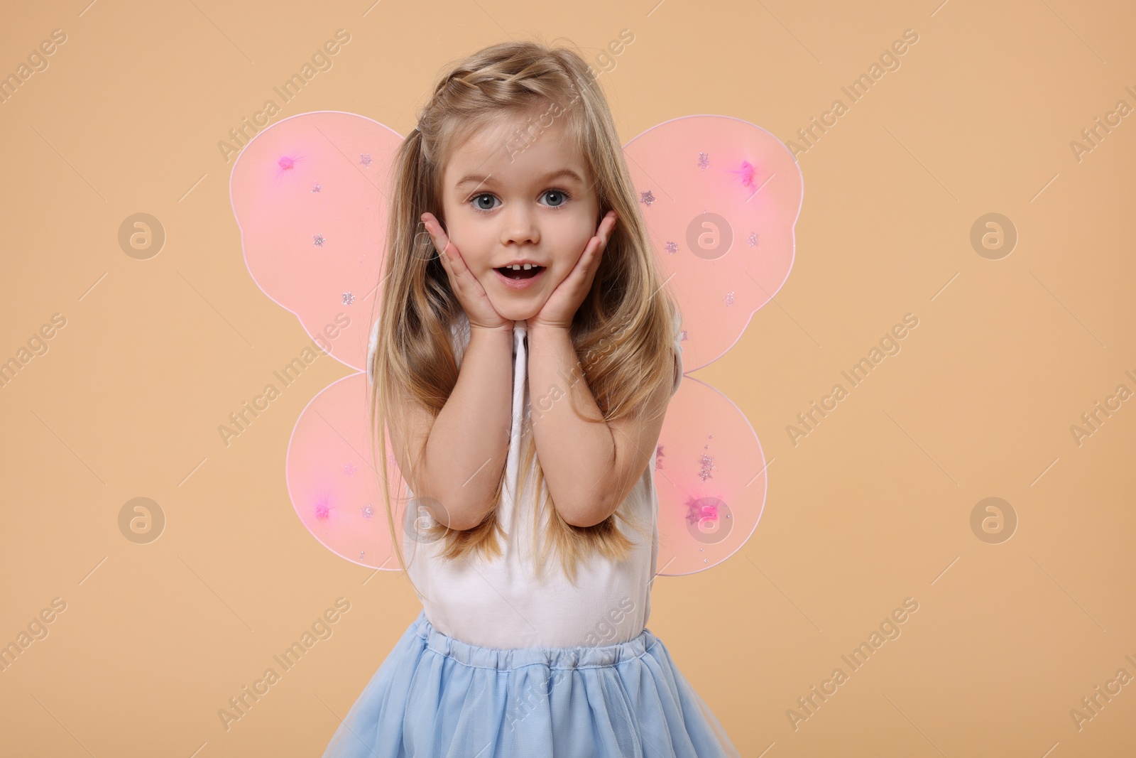 Photo of Cute little girl in fairy costume with pink wings on beige background