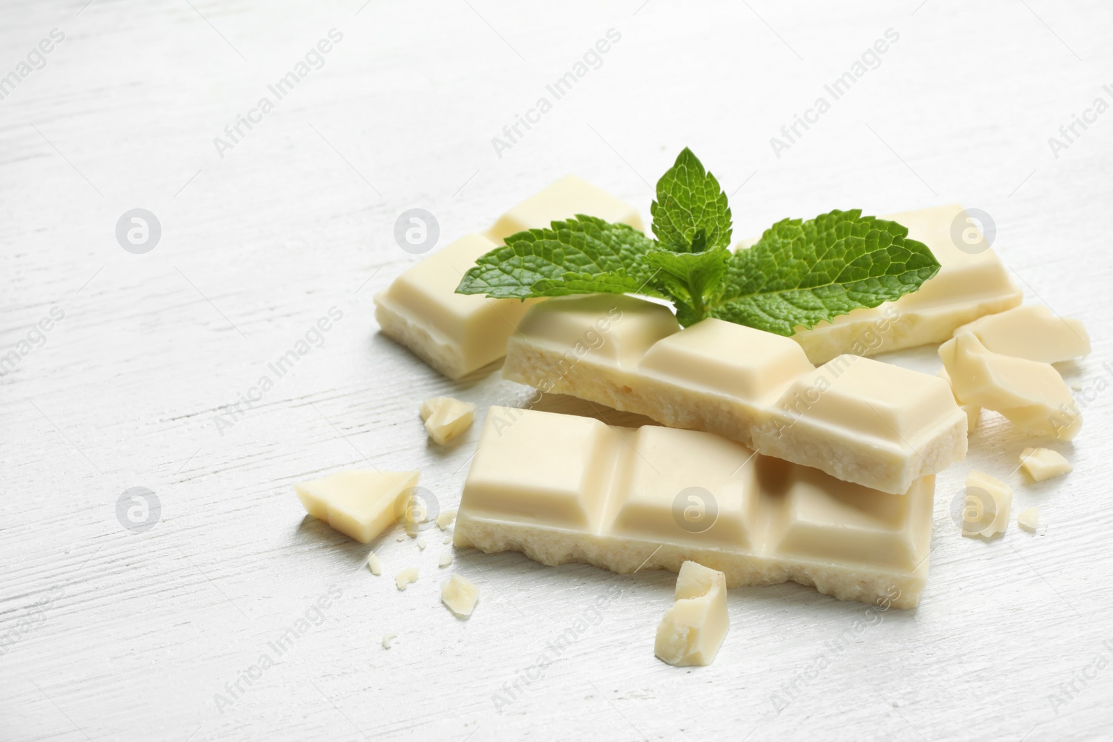 Photo of Pieces of white chocolate with mint on light table