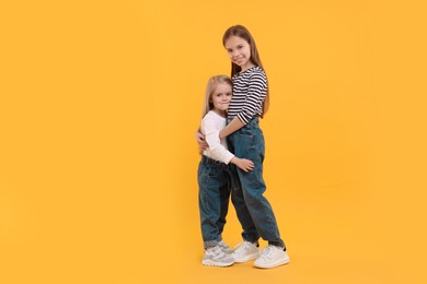 Photo of Full length portrait of cute little sisters on orange background, space for text