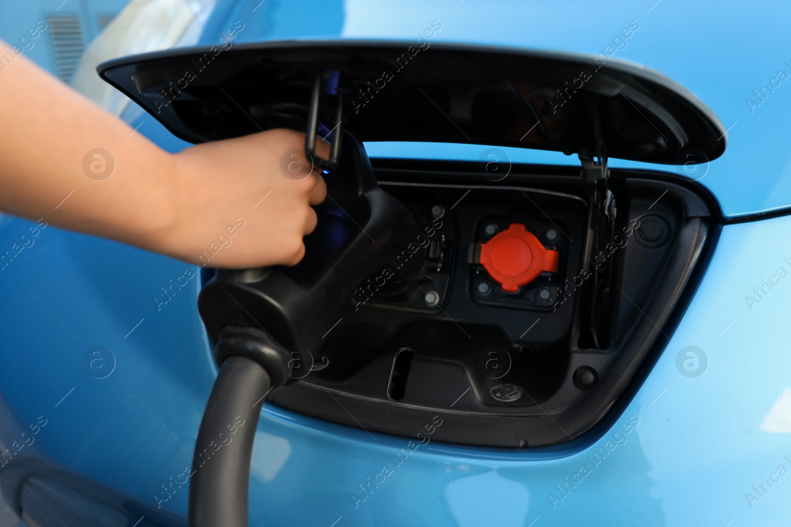 Photo of Woman inserting plug into electric car socket at charging station, closeup