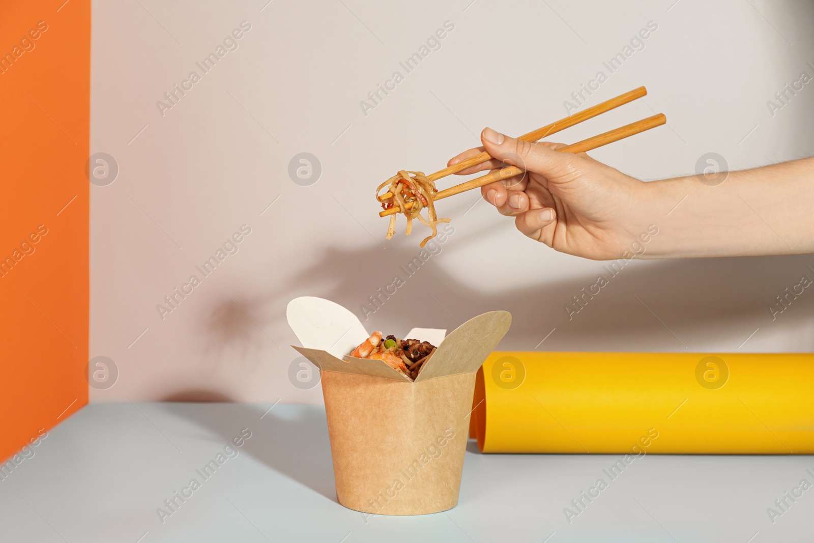 Photo of Woman eating seafood wok noodles with chopsticks from box on color background, closeup