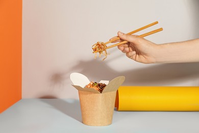 Woman eating seafood wok noodles with chopsticks from box on color background, closeup