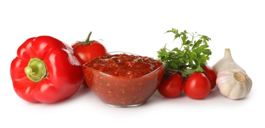 Photo of Glass bowl of tasty adjika and ingredients on white background