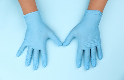 Photo of Person in latex gloves against light blue background, closeup on hands