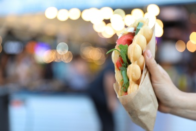 Photo of Young woman holding delicious bubble waffle with tomato and arugula outdoors, closeup