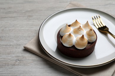 Photo of Delicious salted caramel chocolate tart with meringue served on light beige wooden table, closeup. Space for text