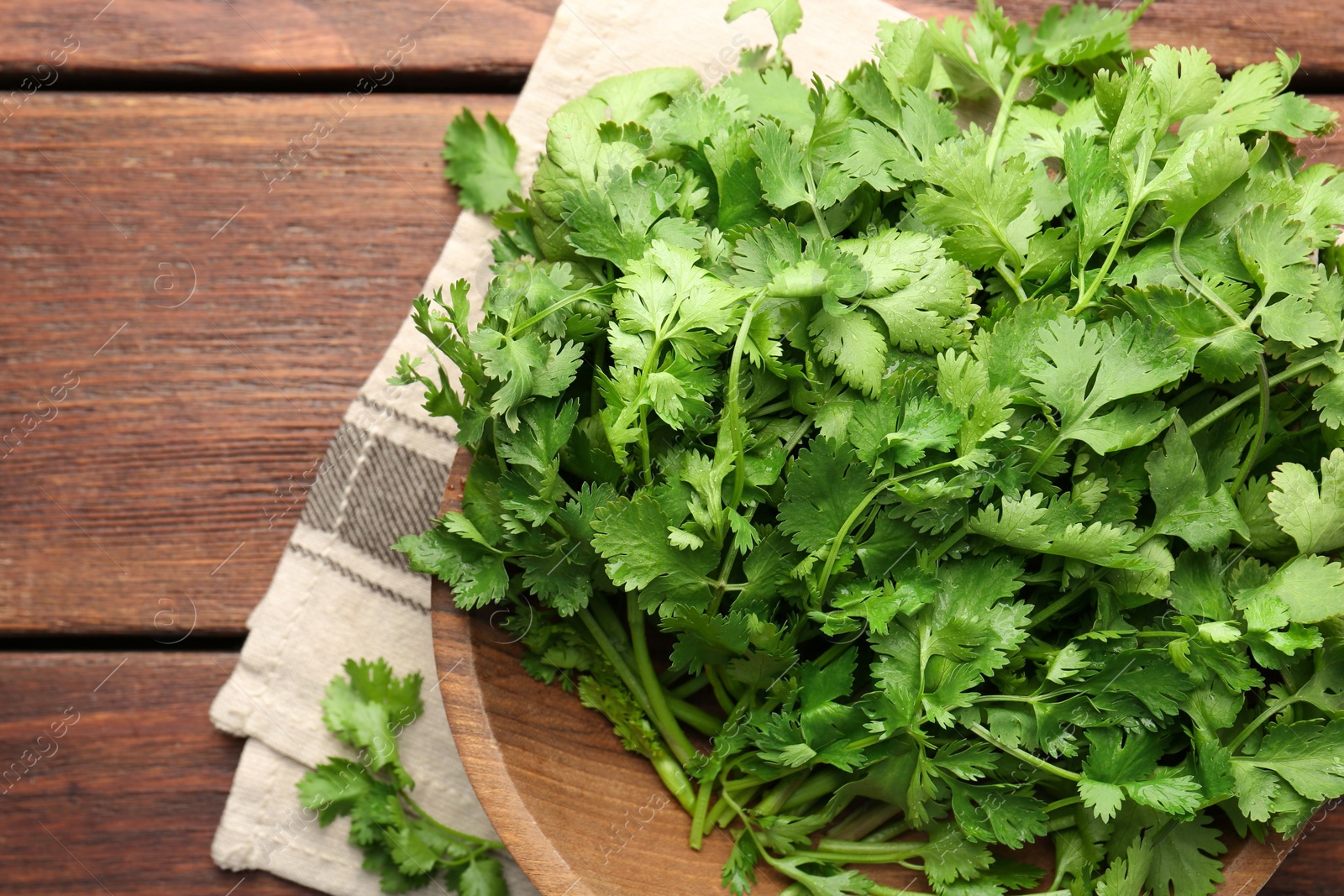 Photo of Fresh coriander in bowl on wooden table, top view