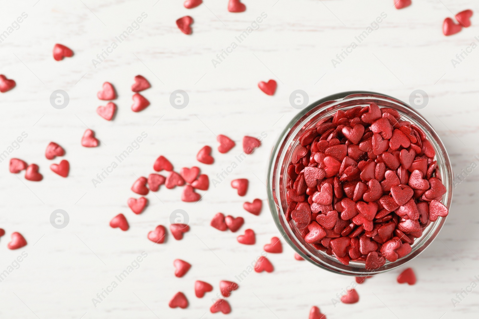 Photo of Bright heart shaped sprinkles and glass bowl on white wooden table, flat lay. Space for text