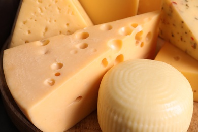 Photo of Different kinds of tasty cheese on wooden plate, closeup