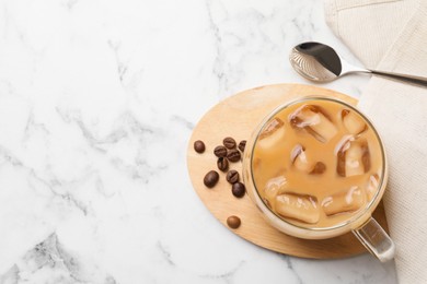 Photo of Refreshing iced coffee with milk in glass cup, beans and spoon on white marble table, flat lay. Space for text