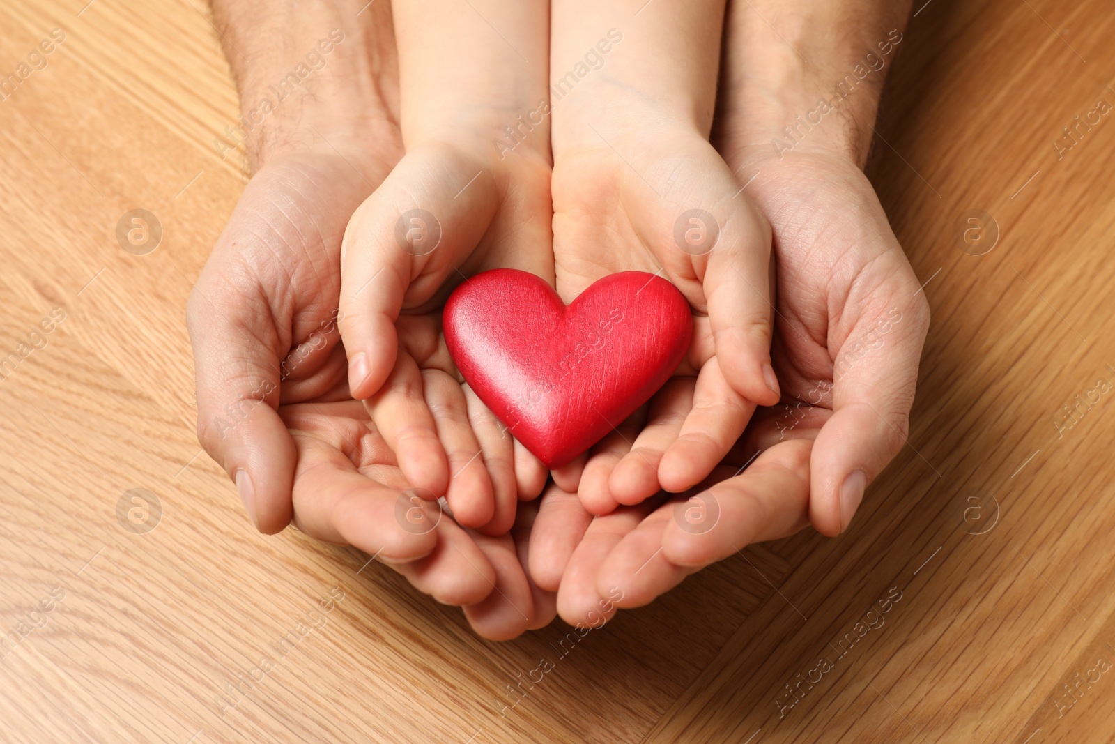 Photo of Man and kid holding red heart in hands at wooden table, closeup