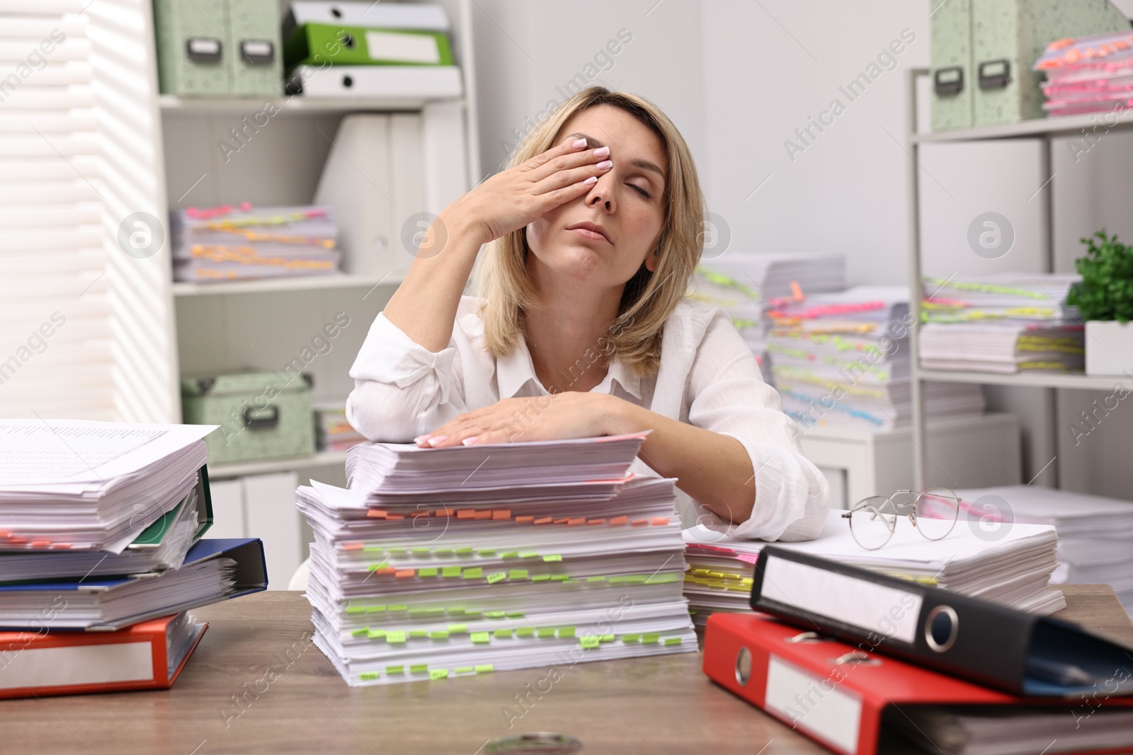 Photo of Overwhelmed woman surrounded by documents at workplace in office