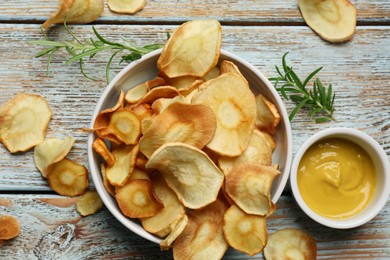 Photo of Tasty homemade parsnip chips with sauce and rosemary on old light blue wooden table, flat lay