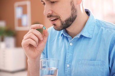 Young man with pill and glass of water indoors