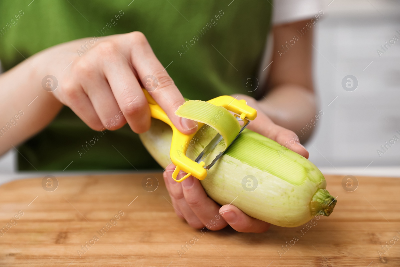 Photo of Woman peeling zucchini at table in kitchen, closeup. Preparing vegetable