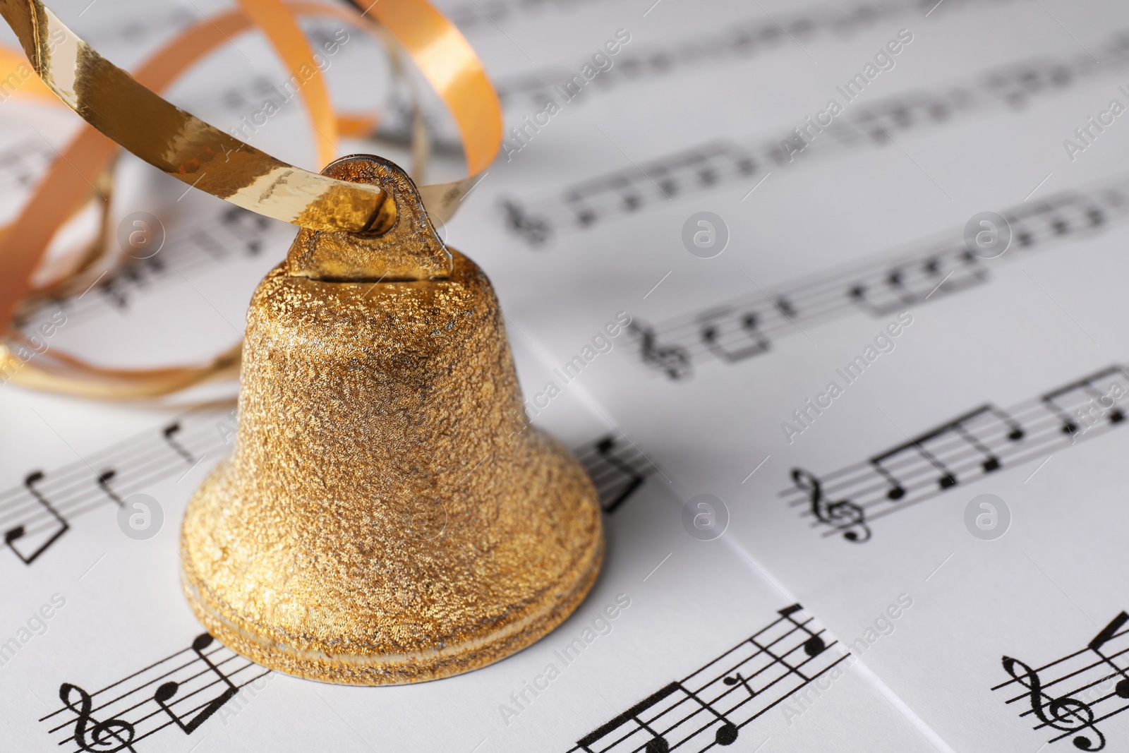 Photo of Golden bell on music sheets, closeup with space for text. Christmas decor