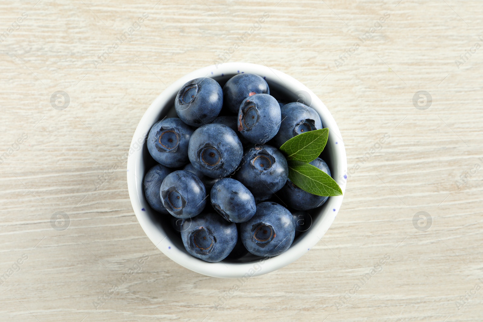 Photo of Bowl of fresh tasty blueberries on white wooden table, top view