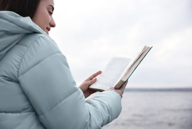 Woman reading book near river on cloudy day