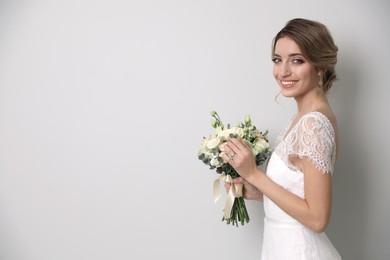 Young bride with beautiful wedding bouquet on light grey background. Space for text