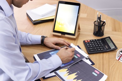 Photo of Businessman working with tablet and charts at table, closeup. Forex trading