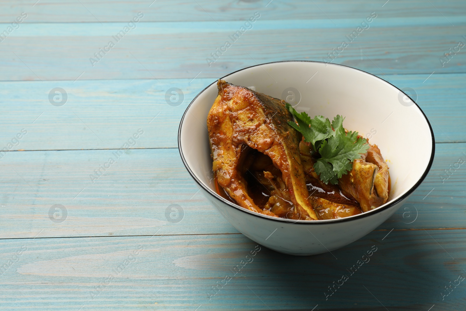 Photo of Tasty fish curry on light blue wooden table, space for text. Indian cuisine