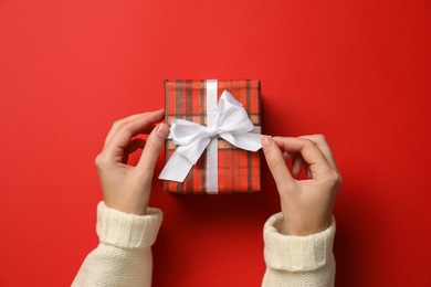 Woman with Christmas gift on red background, top view