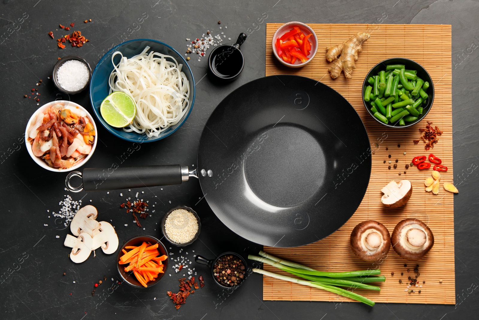 Photo of Flat lay composition with black wok surrounded by spices and products on dark table