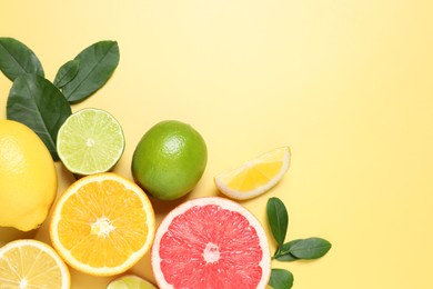 Photo of Different cut and whole citrus fruits on yellow table, flat lay. Space for text