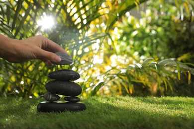 Photo of Woman stacking stones on green grass in garden, closeup. Space for text