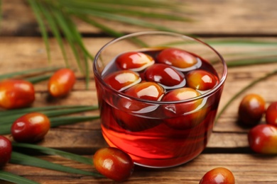 Palm oil in glass with fruits and tropical leaves on wooden table, closeup