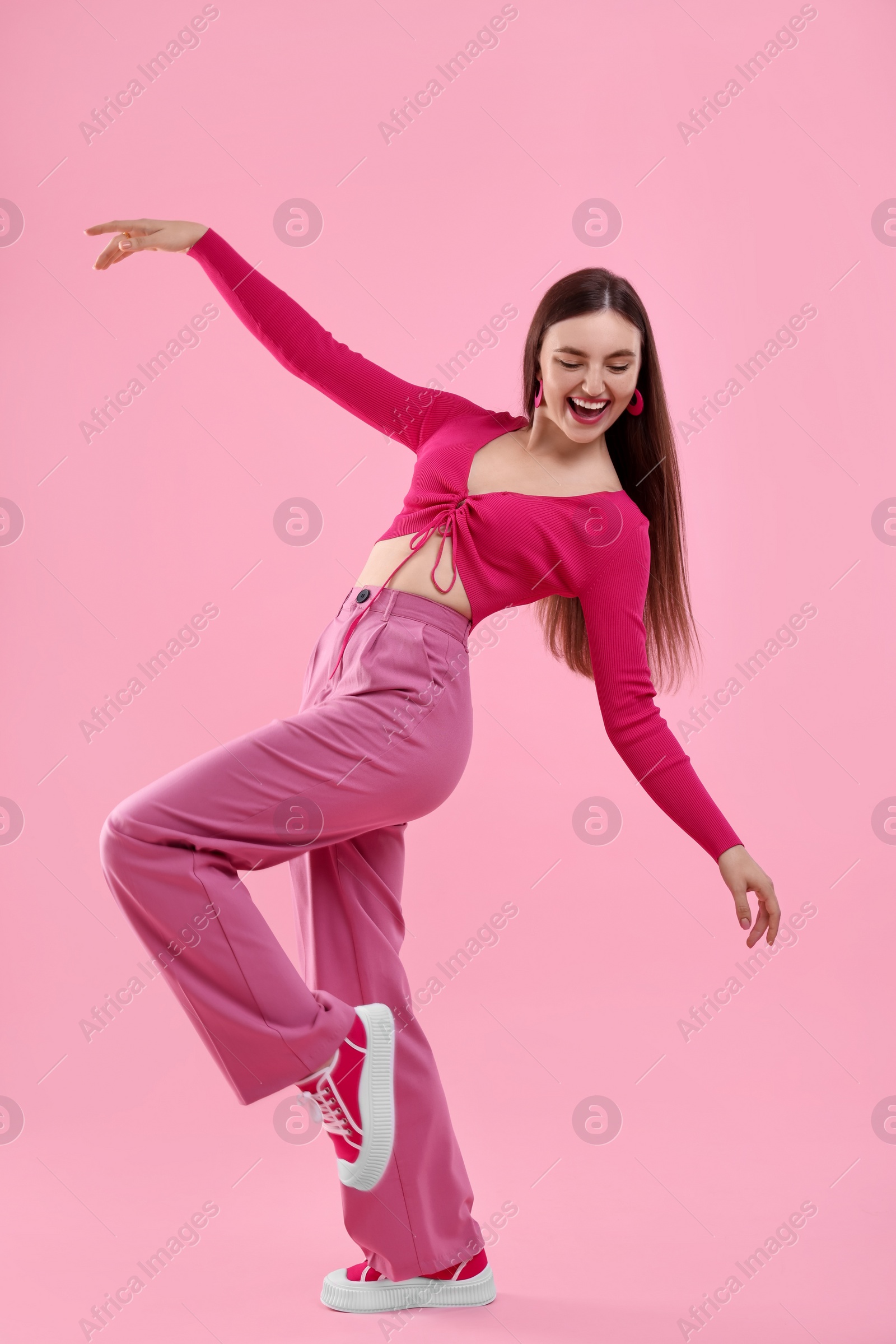 Photo of Beautiful young woman in pink clothes dancing on color background