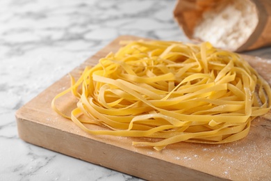 Photo of Wooden board with raw egg noodles on marble table, closeup