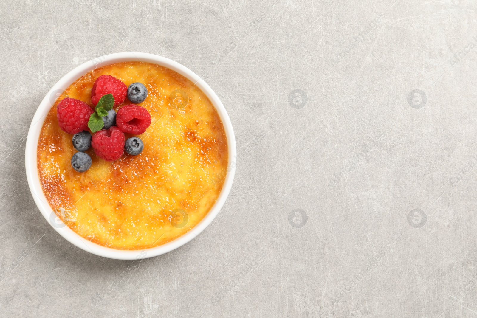 Photo of Delicious creme brulee with fresh berries on light grey table, top view. Space for text
