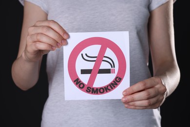 Photo of Woman holding card with no smoking sign on black background, closeup