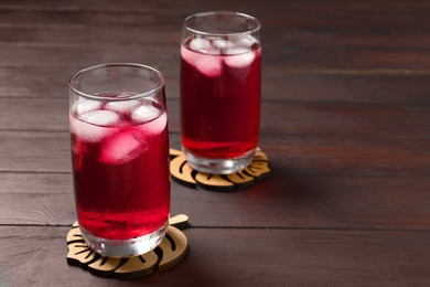 Refreshing hibiscus tea with ice cubes in glasses on wooden table. Space for text
