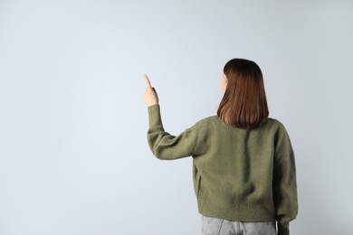 Photo of Young girl pointing on white background, back view. Space for text