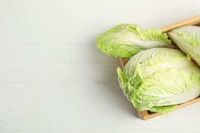 Photo of Chinese cabbages in wooden crate on white table, top view. Space for text