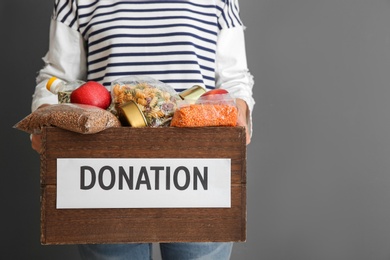 Photo of Person holding donation box with food on gray background, closeup