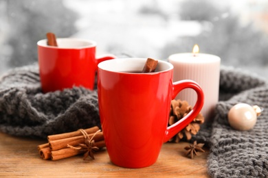 Cups of hot winter drink with scarf on window sill indoors