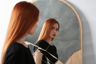 Mental problems. Depressed young woman looking at herself in broken mirror indoors