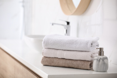 Photo of Stack of fresh towels and soap dispenser on countertop in bathroom
