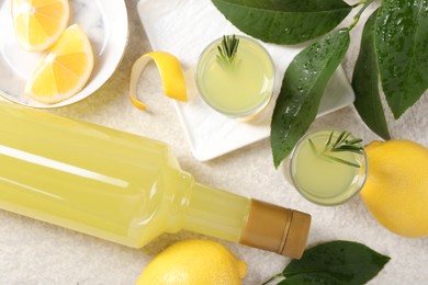 Photo of Tasty limoncello liqueur, lemons and green leaves on light textured table, flat lay