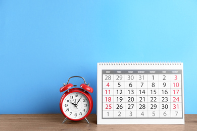 Calendar and alarm clock on wooden table against light blue background