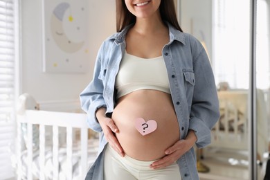 Photo of Pregnant woman with heart shaped sticky note on belly at home, closeup. Choosing baby name
