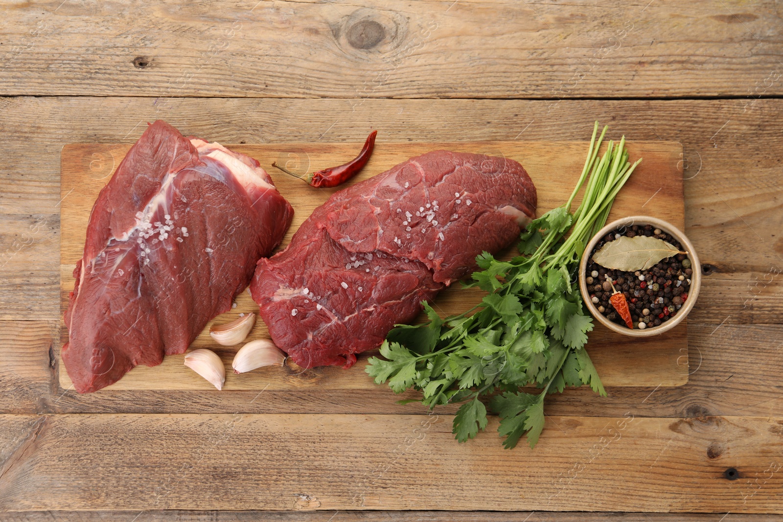 Photo of Pieces of raw beef meat, parsley, garlic and spices on wooden table, top view